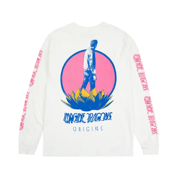 White long sleeve Imagine Dragons Origins tour shirt featuring a stylized graphic of a person standing on a large plant with a pink circular backdrop The bands name Imagine Dragons appears in bold blue text below the design with Origins written underneath in a smaller font The sleeves have repeating pink Imagine Dragons text along their length